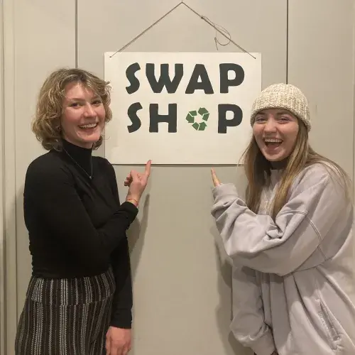 GO Scholar Skylar + volunteer Siri pose with the Swap Shop sign 